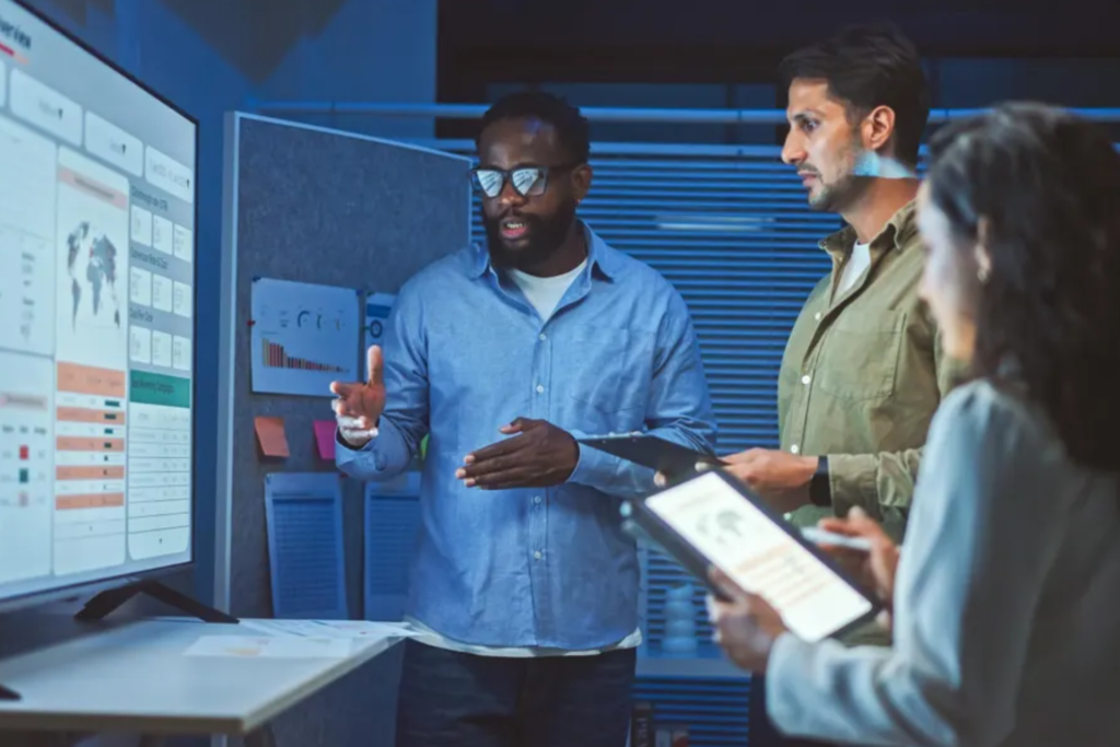 Group of people discuss data-driven research around a large screen, with a man pointing at insights on mobility investing