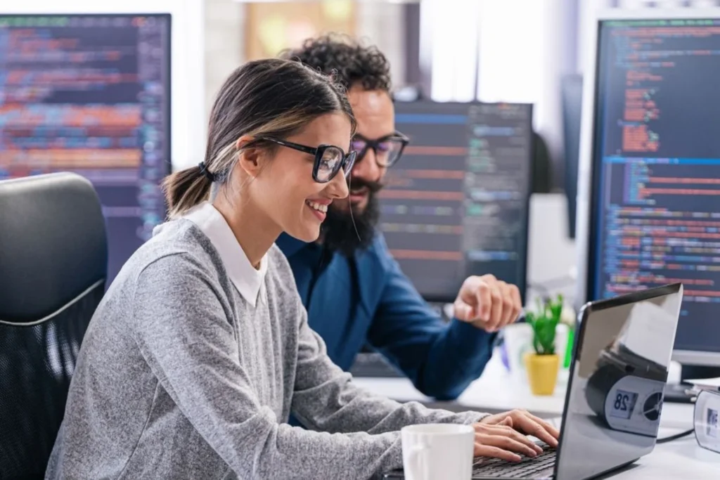 Two colleagues collaborating on a computer in an office setting, focused on a Validation Through Controlled Deployment